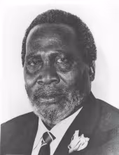 Black-and-white close-up portrait photo of President Jomo Kenyatta wearing a suit, striped tie, and lapel flower, looking directly at the camera.